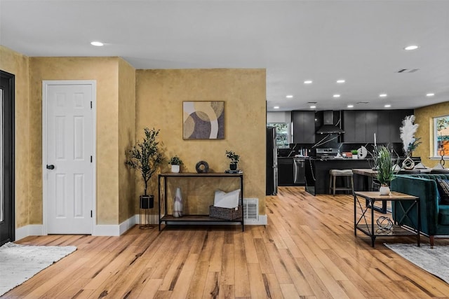 interior space featuring backsplash, light hardwood / wood-style floors, wall chimney exhaust hood, and appliances with stainless steel finishes