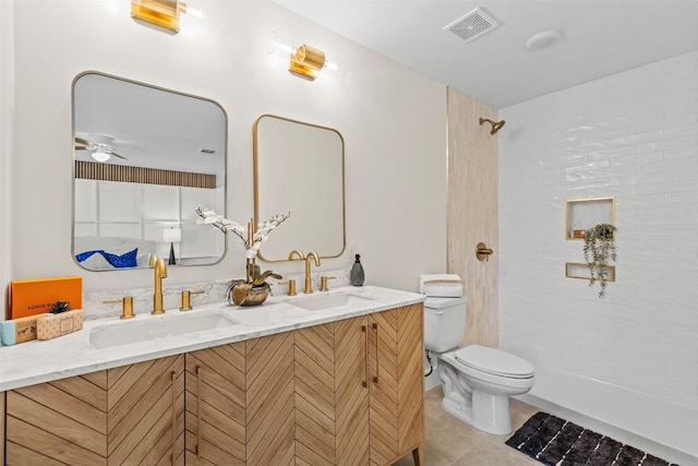 bathroom with tile patterned floors, toilet, a tile shower, vanity, and ceiling fan