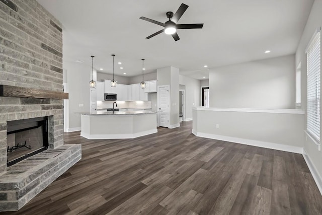 unfurnished living room with dark hardwood / wood-style floors, ceiling fan, a fireplace, and sink