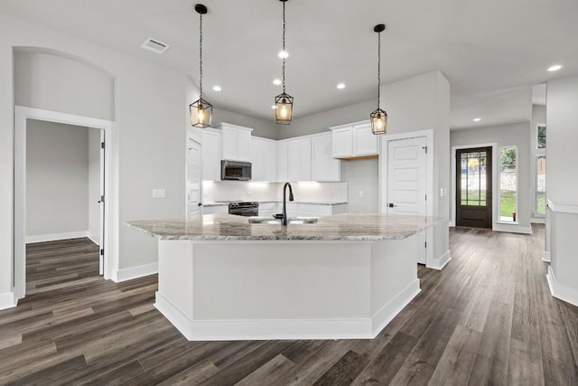 kitchen with white cabinetry, light stone countertops, sink, and a center island with sink