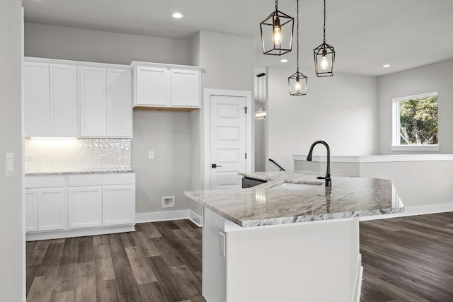 kitchen featuring an island with sink, sink, hanging light fixtures, and white cabinets