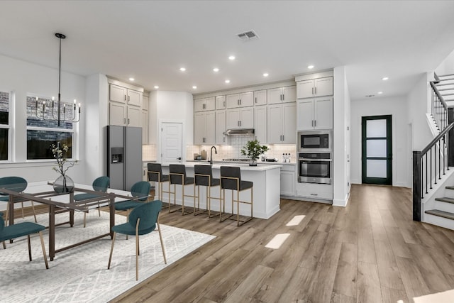 kitchen featuring appliances with stainless steel finishes, a breakfast bar, decorative light fixtures, an island with sink, and backsplash