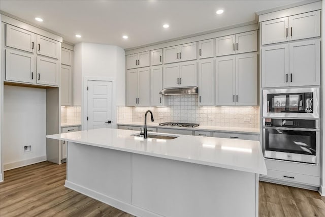 kitchen featuring sink, hardwood / wood-style flooring, appliances with stainless steel finishes, tasteful backsplash, and an island with sink