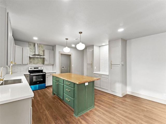 kitchen featuring sink, butcher block countertops, stainless steel electric range oven, a center island, and wall chimney range hood