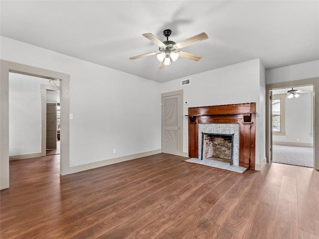 unfurnished living room featuring hardwood / wood-style flooring, ceiling fan, and a tiled fireplace