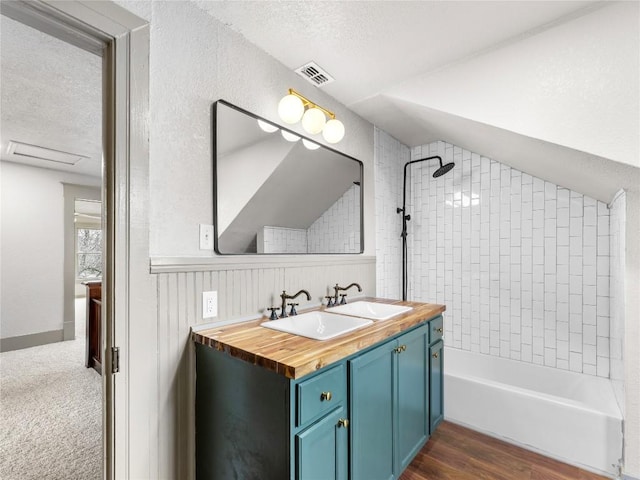 bathroom featuring hardwood / wood-style flooring, vanity, a textured ceiling, vaulted ceiling, and tiled shower / bath