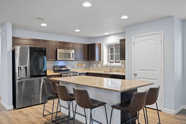 kitchen featuring sink, backsplash, stainless steel appliances, light hardwood / wood-style floors, and a kitchen island