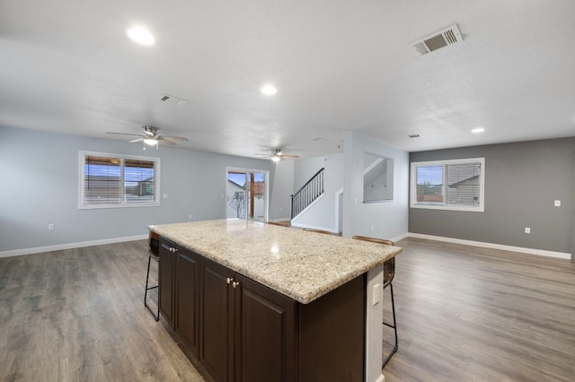 kitchen with dark hardwood / wood-style floors, a kitchen island with sink, a breakfast bar area, and dark brown cabinetry