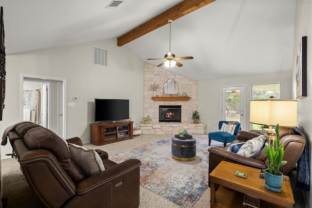 carpeted living room featuring a stone fireplace, lofted ceiling with beams, and ceiling fan