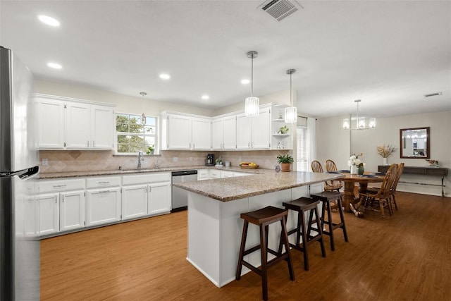 kitchen with a breakfast bar area, white cabinetry, light stone counters, hanging light fixtures, and stainless steel appliances