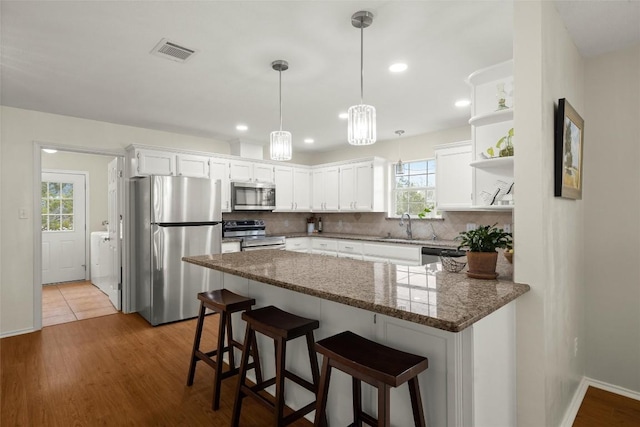 kitchen with appliances with stainless steel finishes, tasteful backsplash, white cabinets, a kitchen bar, and kitchen peninsula