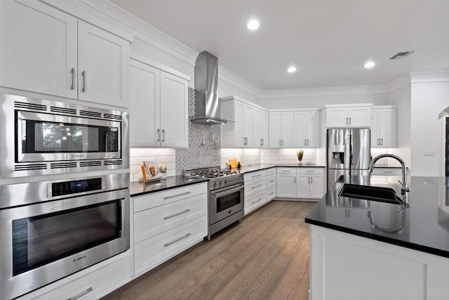 kitchen with appliances with stainless steel finishes, sink, white cabinets, ornamental molding, and wall chimney exhaust hood