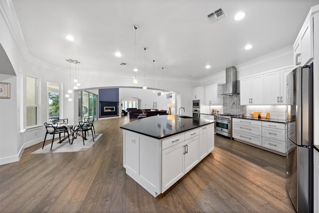 kitchen with a center island with sink, wall chimney range hood, pendant lighting, stainless steel appliances, and white cabinets