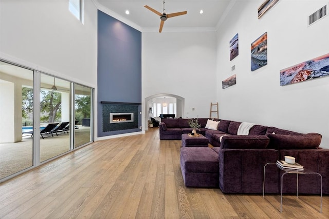 living room with crown molding, ceiling fan, light hardwood / wood-style flooring, and a high ceiling