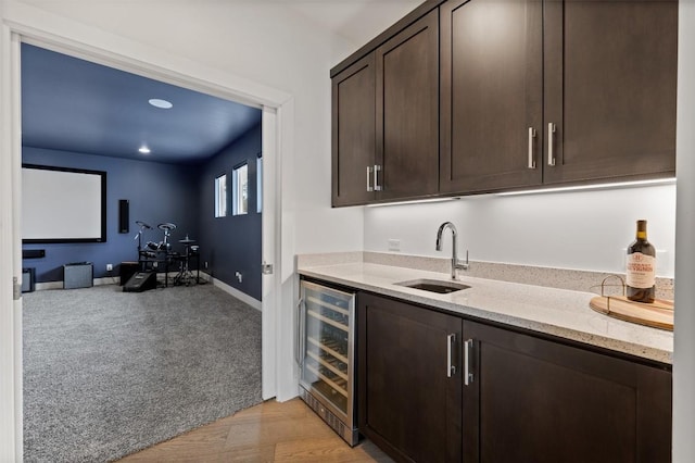 bar featuring sink, wine cooler, dark brown cabinetry, light stone countertops, and light wood-type flooring