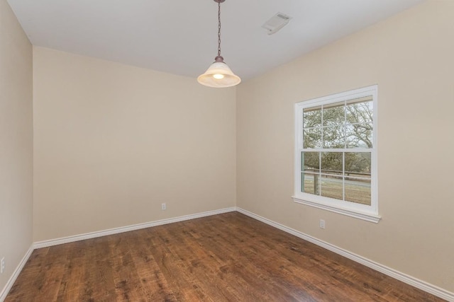 empty room featuring dark wood-style flooring, visible vents, and baseboards