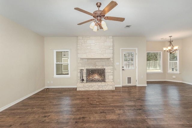 unfurnished living room featuring visible vents, dark wood-type flooring, a stone fireplace, baseboards, and ceiling fan with notable chandelier