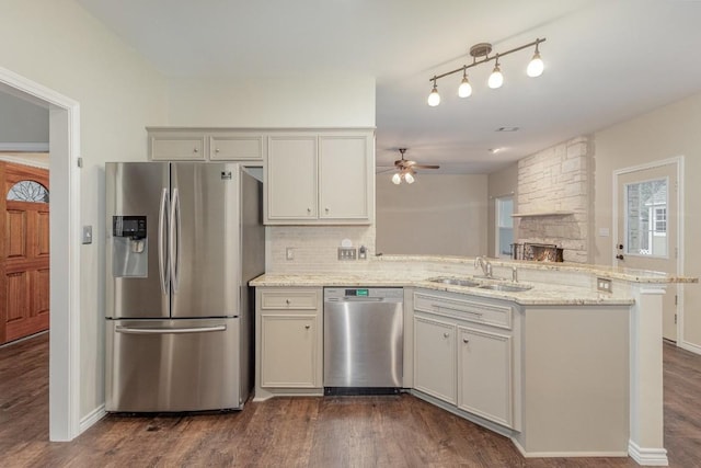 kitchen featuring a peninsula, dark wood-type flooring, a sink, appliances with stainless steel finishes, and decorative backsplash