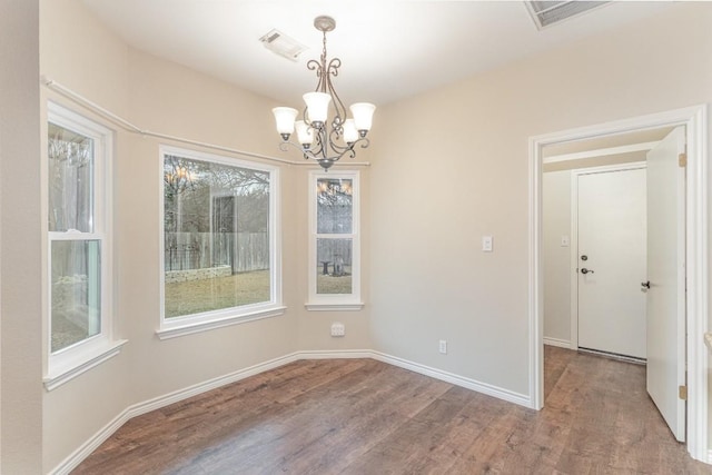 unfurnished dining area with baseboards, visible vents, a chandelier, and wood finished floors