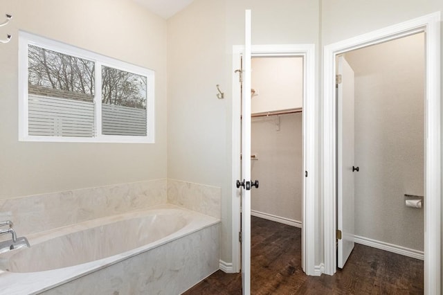 bathroom with a garden tub, a spacious closet, baseboards, and wood finished floors