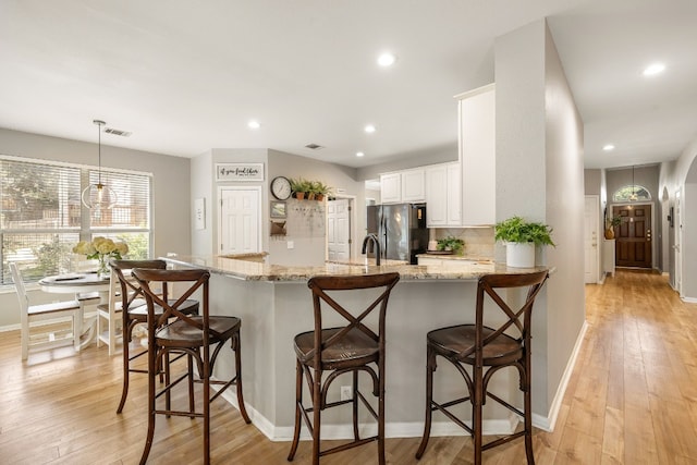 kitchen with hanging light fixtures, stainless steel fridge, kitchen peninsula, a kitchen breakfast bar, and light stone countertops