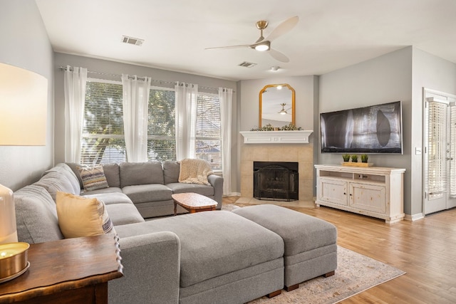 living room featuring light hardwood / wood-style flooring, a tile fireplace, and ceiling fan