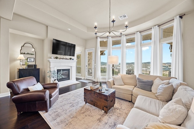 living room with wood finished floors, visible vents, baseboards, a raised ceiling, and a glass covered fireplace