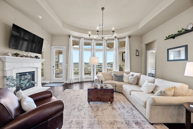 living room with plenty of natural light, a tray ceiling, wood finished floors, and a glass covered fireplace