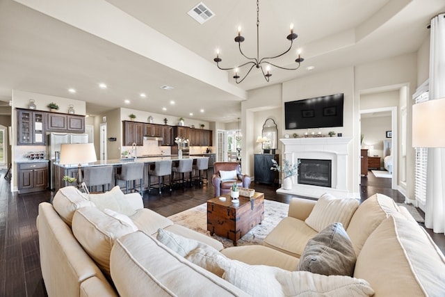 living room with dark wood finished floors, a glass covered fireplace, visible vents, and recessed lighting