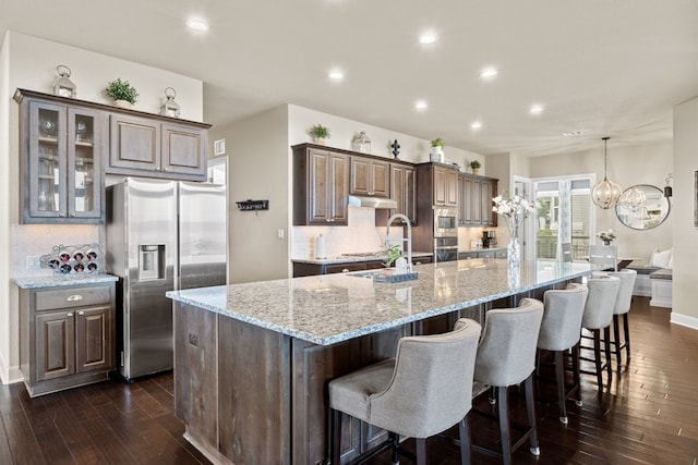 kitchen with appliances with stainless steel finishes, dark wood-style flooring, decorative backsplash, and under cabinet range hood