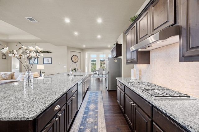 kitchen with dark brown cabinetry, under cabinet range hood, a sink, appliances with stainless steel finishes, and dark wood-style floors