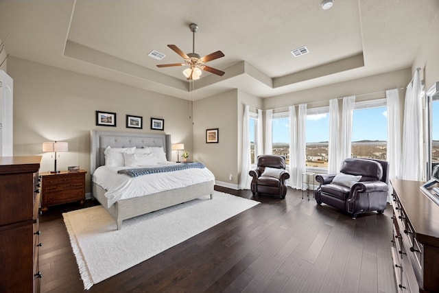 bedroom featuring a tray ceiling, dark wood-style flooring, visible vents, and baseboards