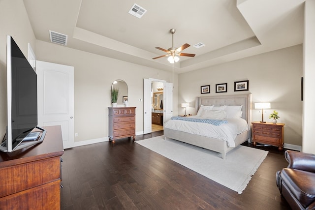 bedroom with a tray ceiling, dark wood finished floors, and visible vents