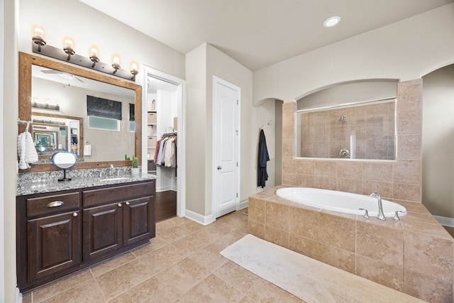 bathroom with a tile shower, vanity, baseboards, and a bath