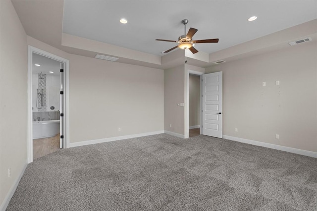 unfurnished bedroom featuring a raised ceiling, carpet floors, and connected bathroom