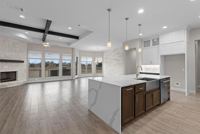 kitchen with a stone fireplace, sink, white cabinetry, light stone counters, and pendant lighting