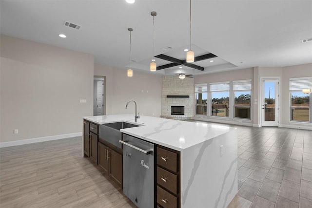 kitchen featuring hanging light fixtures, stainless steel dishwasher, a large fireplace, an island with sink, and light stone countertops