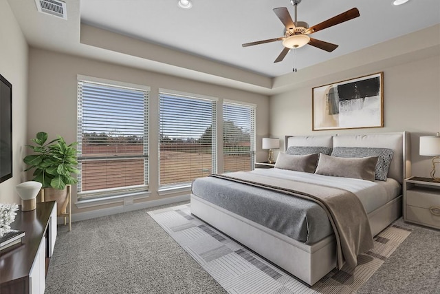 carpeted bedroom with ceiling fan and a tray ceiling