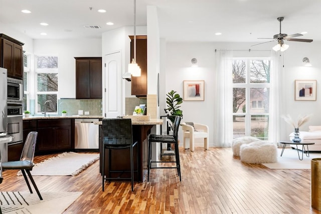 kitchen with appliances with stainless steel finishes, light stone counters, tasteful backsplash, a kitchen bar, and decorative light fixtures