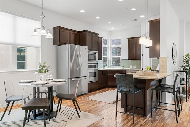 kitchen featuring light stone countertops, decorative light fixtures, stainless steel appliances, and light hardwood / wood-style floors