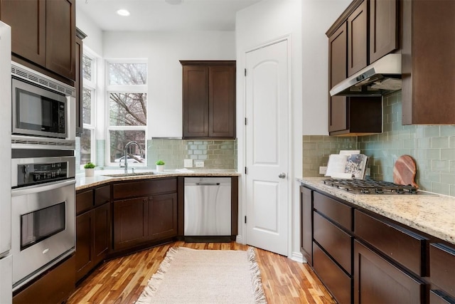 kitchen with stainless steel appliances, sink, dark brown cabinetry, and light stone counters