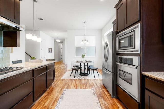 kitchen featuring decorative light fixtures, dark brown cabinetry, stainless steel appliances, light stone countertops, and light wood-type flooring