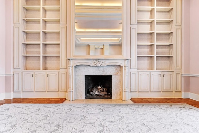 unfurnished living room featuring light wood-type flooring, a premium fireplace, baseboards, and built in features