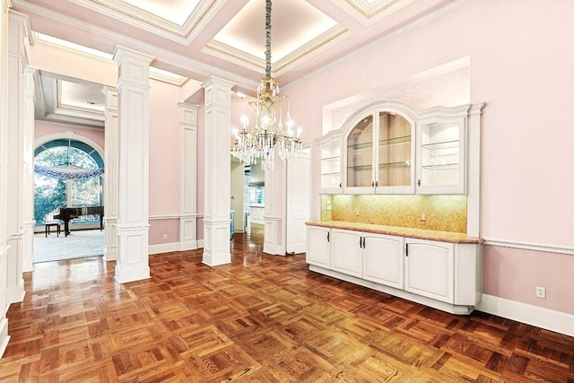 unfurnished dining area with decorative columns, healthy amount of natural light, ornamental molding, a chandelier, and a high ceiling