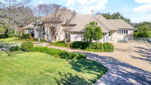 view of front facade featuring metal roof, fence, driveway, a standing seam roof, and a chimney