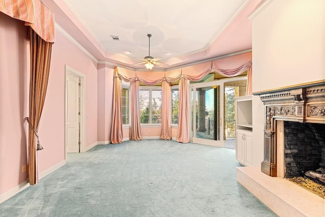 unfurnished living room featuring carpet flooring, a raised ceiling, a premium fireplace, crown molding, and a ceiling fan