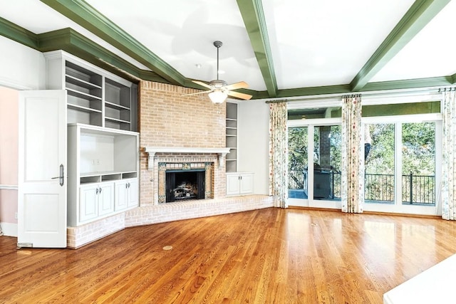 unfurnished living room featuring a ceiling fan, beamed ceiling, wood finished floors, a brick fireplace, and built in shelves