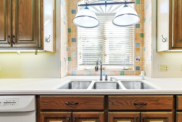 kitchen with dishwasher, light countertops, a sink, and brown cabinets