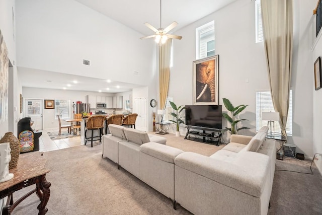 carpeted living room featuring ceiling fan, plenty of natural light, and a high ceiling