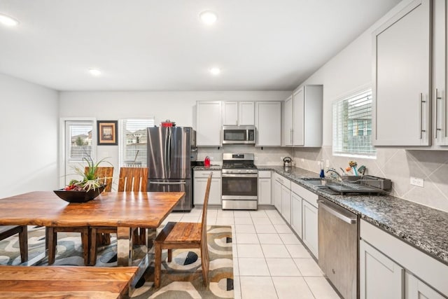 kitchen featuring light tile patterned floors, dark stone countertops, a wealth of natural light, stainless steel appliances, and decorative backsplash